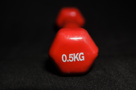 little red dumbbell isolated on black background weighting 0.5 kilograms. sport equipment, fitness item with copy space. Healthy lifestyle and weight loss conceptの写真素材