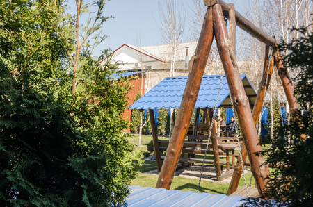 view from the back yard at home at summer season. Landscape design works. Green plants, fir trees and stones in blooming garden. Wooden swings and arbourの写真素材
