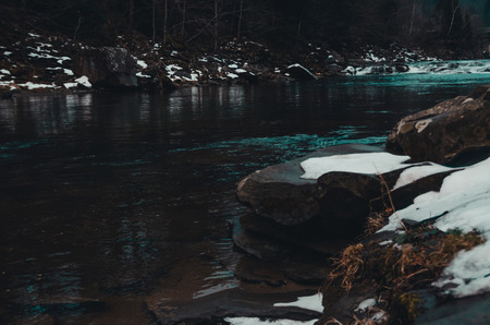 river in the mountains with swirling stream of water. Big boulders in mountain creek background.  fast flow near wet stones covered with snow. Bukovel, Ukraine in winter seasonの写真素材