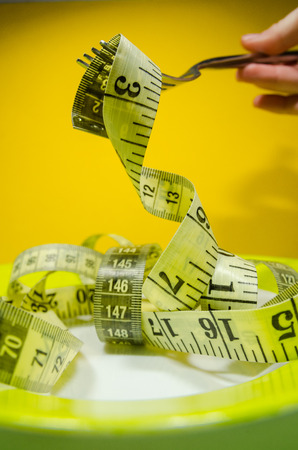 a plate and a silver fork with yellow measuring tape. Diet and nutrition plan concept.の写真素材