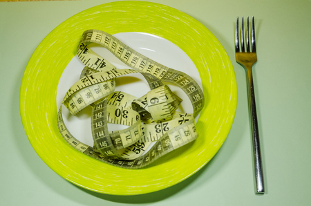 a plate and a silver fork with yellow measuring tape. Diet and nutrition plan concept.の写真素材