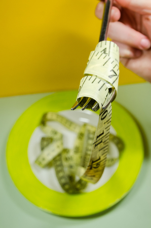 a plate and a silver fork with yellow measuring tape. Diet and nutrition plan concept.の写真素材
