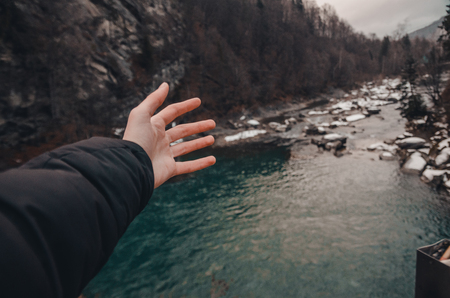 river in the mountains of bukovel with swirling stream of water. Big boulders in mountain creek background. A human hand in front of fast flow near wet stones covered with snow.の写真素材
