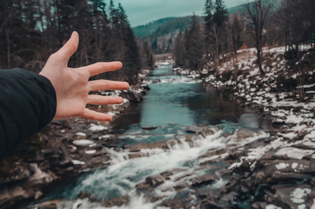 river in the mountains of bukovel with swirling stream of water. Big boulders in mountain creek background. A human hand in front of fast flow near wet stones.の写真素材