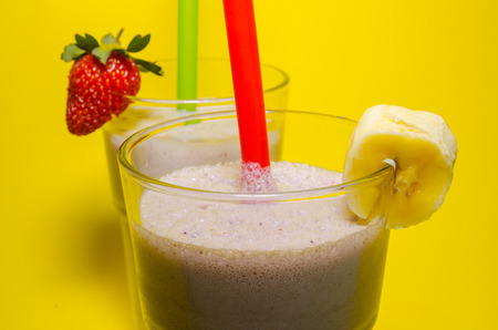 two glass cups of milkshake with straws. Milkshakes with banana and strawberry close upの写真素材