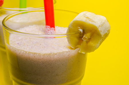 two glass cups of milkshake with straws. Milkshakes with banana and strawberry close upの写真素材