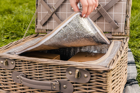 womans hand opening picnic basket with boxes and silver cutlery outside on the grey blanket.の写真素材