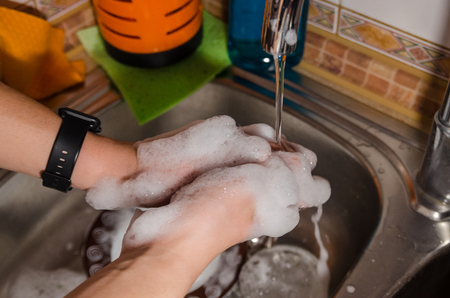 mans hand washing a plate with water from dish soap in the kitchen sinkの写真素材