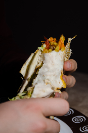 hand holding bitten shawarma with chicken on black background. eating kebab conceptの写真素材