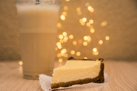 a slice of cheesecake and vanilla milkshake in takeaway cup on wooden table served in coffee shopの写真素材