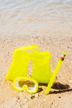 yellow swimming flippers with mask and tube on sand beach by the clear sea