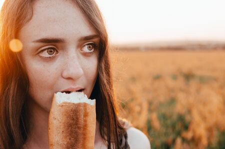 close up view of woman eating french baguette in golden wheat meadowの写真素材