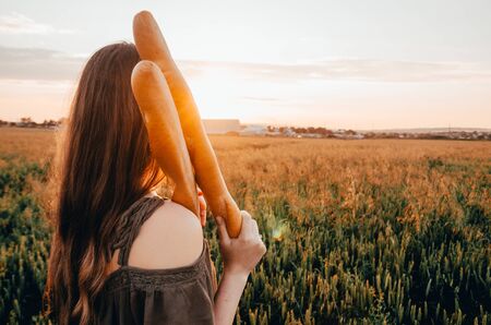 woman holds french baguette in wheat fieldの写真素材
