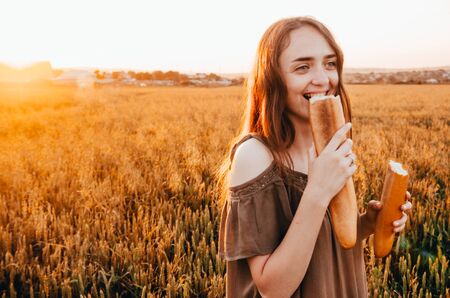 happy woman eating french baguette in golden wheat meadowの写真素材