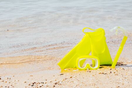 yellow swimming flippers with mask and tube on sand beach by the clear sea