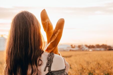 close up photo of woman holds freshmade french baguettes in wheat fieldの写真素材