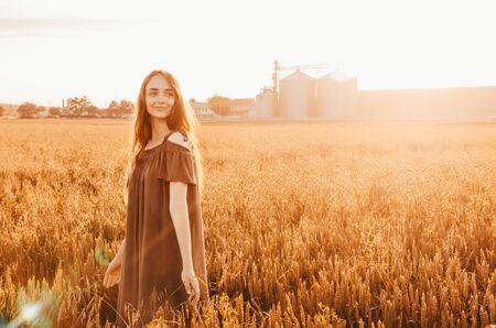 woman in green dress stands smilling in wheat field with shining sunの写真素材