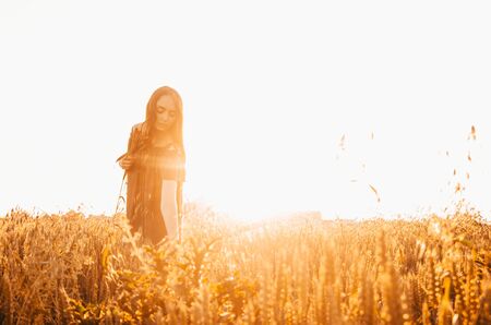 woman in green dress standing in wheat field with shining sunの写真素材