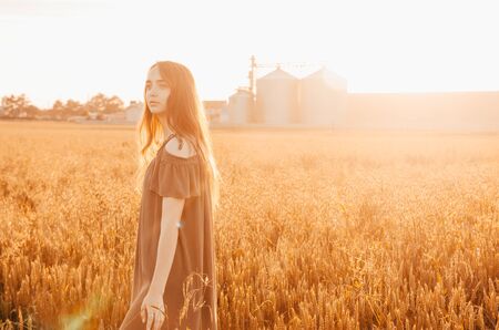 woman in green dress standing in wheat field with shining sunの写真素材