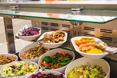 buffet table with salats and  vegetables in big white plates.