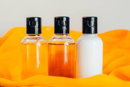 close up view of shower gel, shampoo and body lotion in small travel tubes in hotel bathroom on orange towelの写真素材