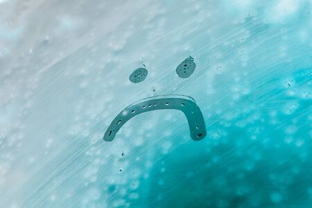 unhappy face on foggy window. rainy weather outsideの写真素材