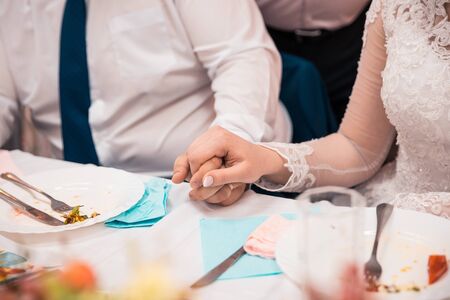 bride and groom holding hands on the table while eating at the wedding dayの写真素材