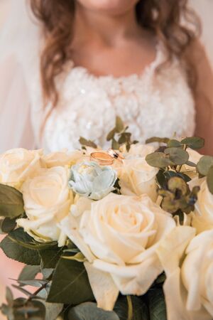 two golden wedding rings lie on the bouquet of flowers with ready bride on the backgroundの写真素材