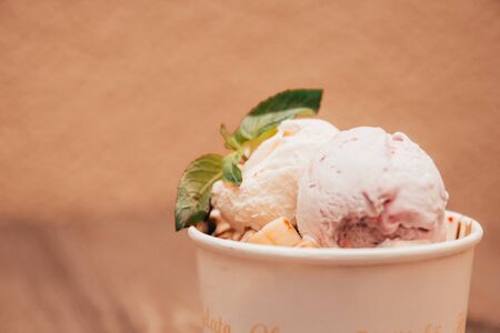 close up view of different flavoured ice cream scoops with sprig of mint and bananas in paper cup. fresh made ice cream with fruits and chocolate toppingの販売画像