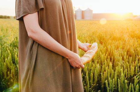 girl in dress walking with french baguette in green wheat fieldの写真素材