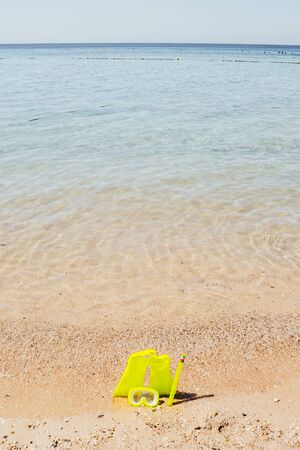 yellow swimming flippers with mask and tube on sand beach by the clear seaの写真素材
