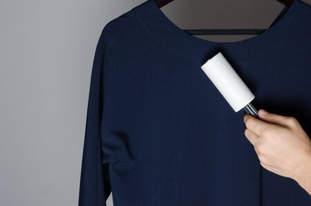 cleaning the dress with adhesive sticky roller. Domestic cleaning tool for getting rid of dandruff, hair, debris, pet wool and fluff. One-time paper roller with adhered dustの写真素材