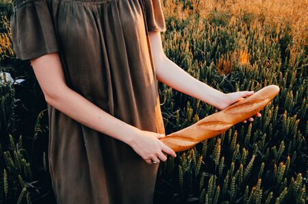 girl in dress walking with french baguette in green wheat fieldの写真素材