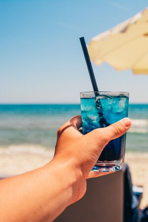 blue refreshing cocktail at the beach in the mans handの写真素材