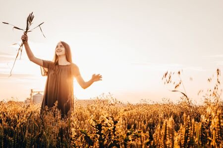 happy woman in green dress standing in wheat fieldの写真素材