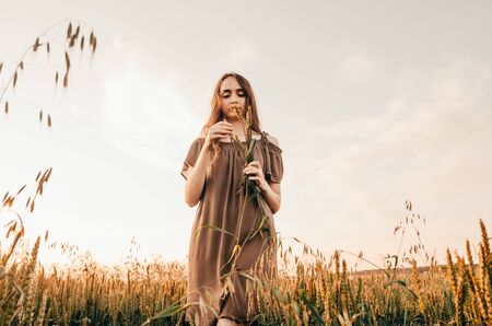 woman in dress standing in green wheat field while sunsetの写真素材