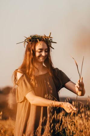 woman in dress and with wreath on her head is standing in wheat fieldの写真素材