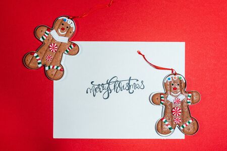 card with merry christmas handwriting on red background decorated with ginger cookiesの写真素材