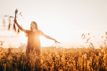 happy woman in green dress stands smilling in wheat field with shining sunの写真素材