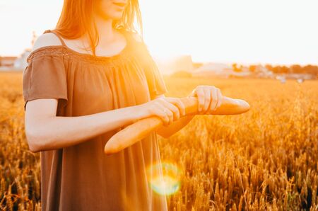 woman eating french baguette in golden wheat meadow with sun raysの写真素材