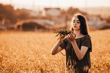 young woman ia making a wreath and is standing in golden wheat fieldの写真素材