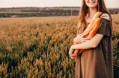 close up photo of woman holds freshmade french baguettes in wheat fieldの写真素材