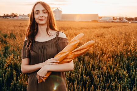 woman holding french baguettes in golden wheat field with sun raysの写真素材