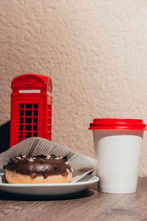 coffee in takeaway cup with chocolate donut. little london telephone box as decor in the coffee shop. having breakfast in london conceptの写真素材