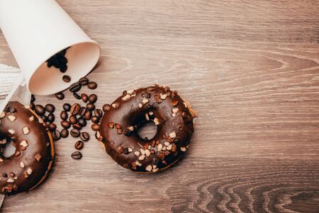 background of takeaway cup with coffe grains and chocolate donuts on the wooden table. flat tay breakfast at the coffee shop concept from top viewの写真素材