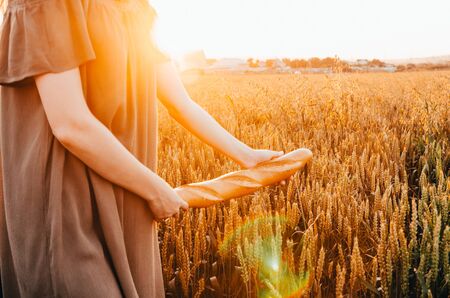 girl in dress walking with french baguette in green wheat fieldの写真素材