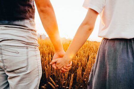 a young couple in wheat field holding hands while sunriseの写真素材