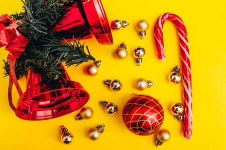 christmas decor on yellow background. christmas tree balls, bell and peppermint candy cane flat lay from top viewの写真素材