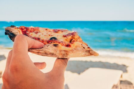 eating a slice of pizza at the sea beach.の写真素材