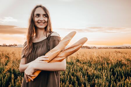 woman in dress standing wheat field with two french baguettesの写真素材